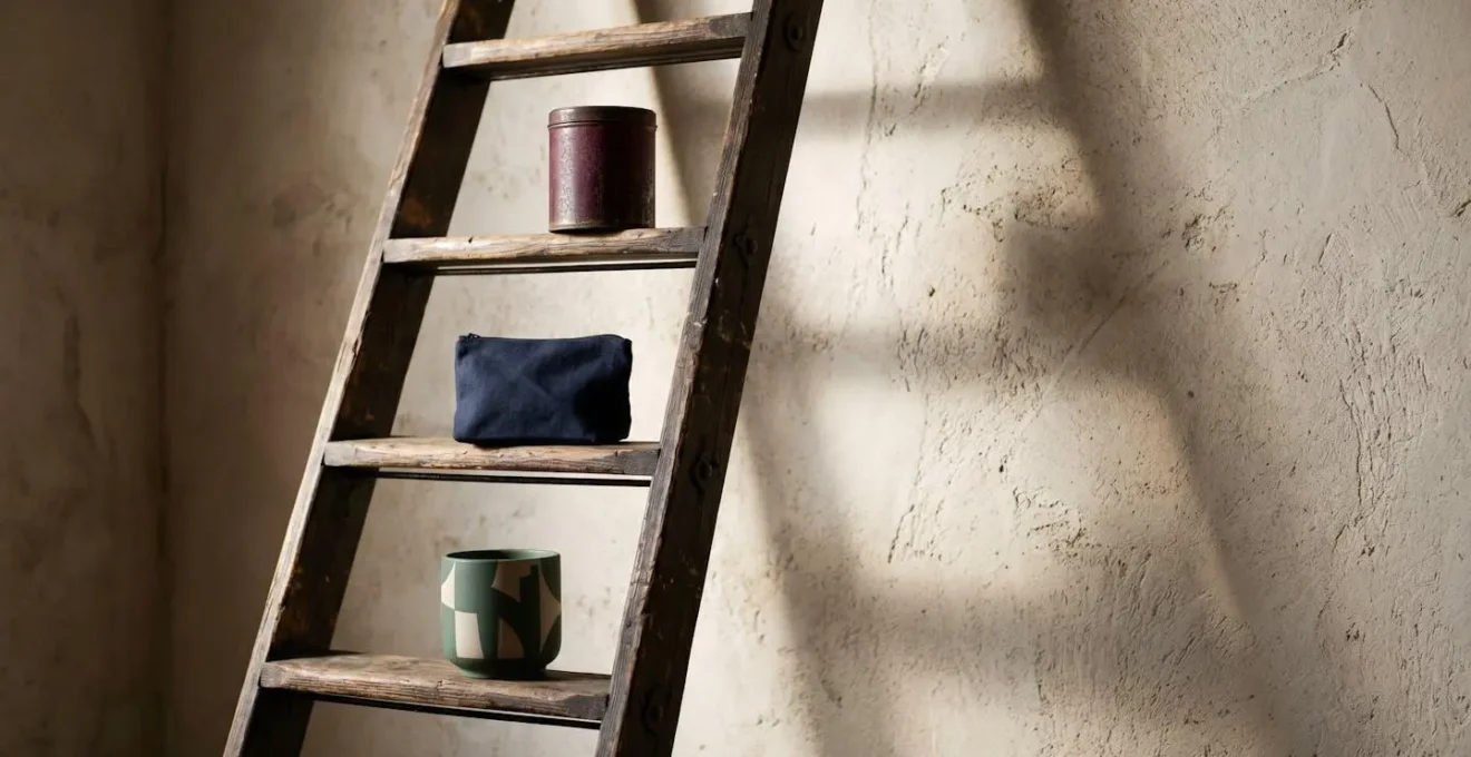 A wooden ladder leans against a textured wall, with small branded metal containers placed on different rungs, symbolizing a staggered savings strategy.